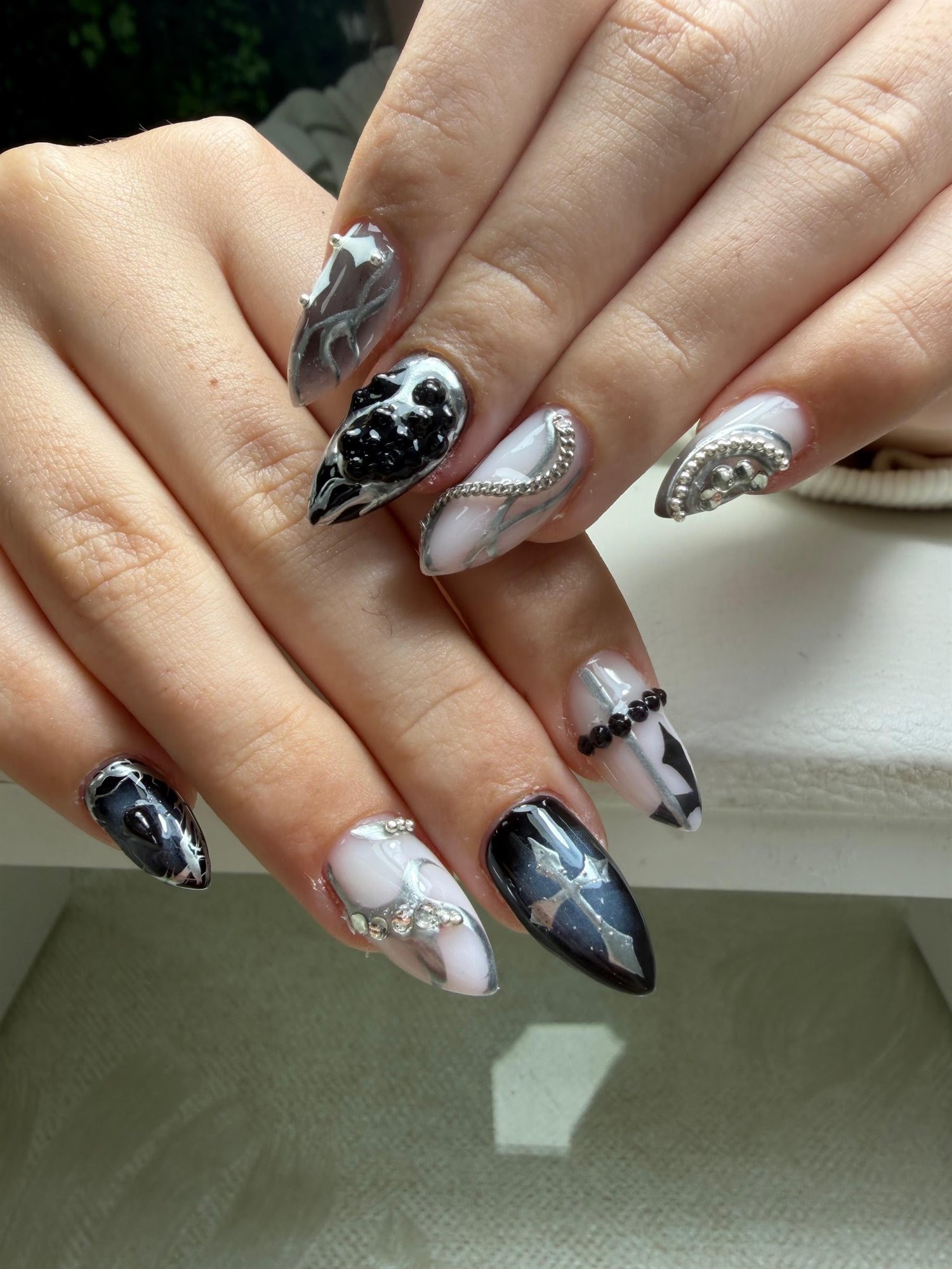 Manos con uñas esculpidas en negro y plata con relieve y pedrería, trabajo de Adenails